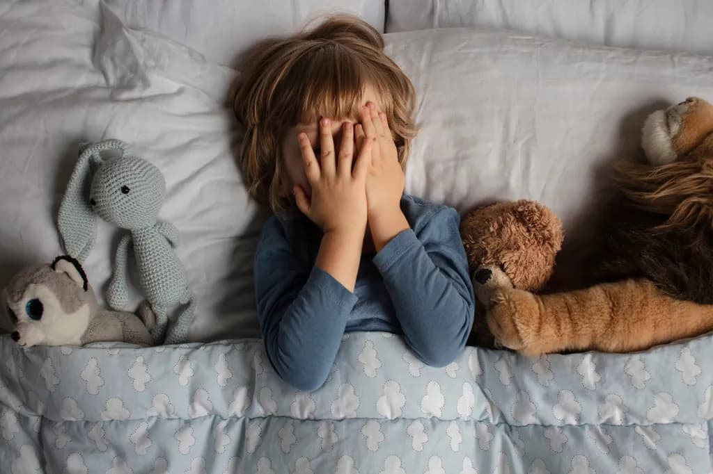 Das Kind hatte Angst, bevor es ins Bett ging. Nachtschrecken in einem Kind. Das Kind bedeckt sein Gesicht mit seinen Händen in Angst.